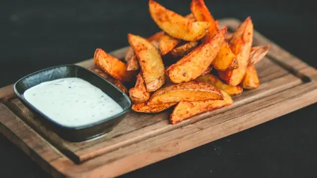 Golden fried potato wedges with creamy dipping sauce on a wooden board