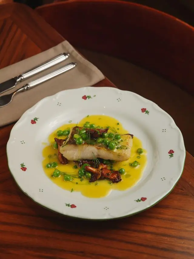 Seared fish fillet with peas, herbs, and golden sauce on a white plate