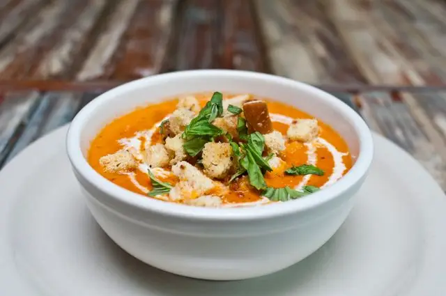 Bowl of tomato soup topped with croutons, cream, and fresh herbs